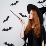 Halloween Concept - Beautiful Witch playing with magic stick on grey background.