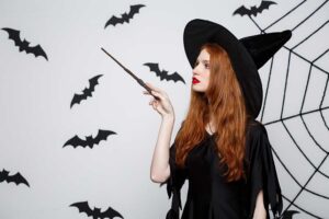 Halloween Concept - Beautiful Witch playing with magic stick on grey background.